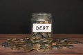 Debt label on coin jar on top of wooden desk with asorted coins background.