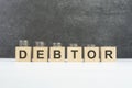 debtor word, text written on wooden cubes on a black background with coins on cubes