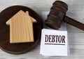 DEBTOR - word on a white sheet against the background of a judge`s hammer and a wooden house