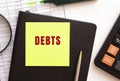 DEBTS text on a sticker on your desktop. Diary, calculator and pen