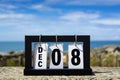 Dec 08 calendar date text on wooden frame with blurred background of ocean.