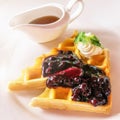 A decadent breakfast plate of Belgian waffles, whipped cream, and maple syrup.