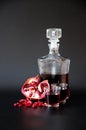 A decanter and two glasses of pomegranate liqueur next to the fruit and fruit seeds on a black background Royalty Free Stock Photo