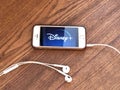 December 2019 Los Angeles: Disney + company logo icon on smartphone screen close-up on wooden table with headphones. Disney + visu