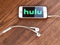 December 2019 Milan, Italy: Hulu company logo icon on smartphone screen close-up on wooden table with headphones. Hulu visual bran