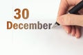December 30th. Day 30 of month, Calendar date. The hand holds a black pen and writes the calendar date. Winter month, day of the
