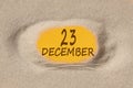 December 23. 23th day of the month, calendar date. Hole in sand. Yellow background is visible through hole