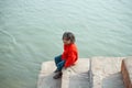 December 17 2019 Varanasi, India. A homeless bored child sitting on the steps near the river. In the background the waters of the