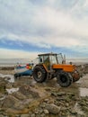 December 2018 - Wissant, France: Orange tractor towing a wooden white and blue fishing boat on a rocky beach during low tide Royalty Free Stock Photo