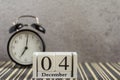 December 4 on a wooden calendar next to an alarm clock on a dark table .One day of winter.Space for text