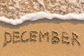 December - word drawn on the sand beach with the soft wave.