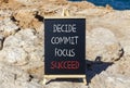 Decide commit focus succeed symbol. Concept word Decide Commit Focus Succeed on beautiful blackboard. Beautiful red stone blue sea Royalty Free Stock Photo