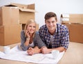 Deciding on the layout of their new flat. A young couple lying on the floor with the blueprints of their new flat and Royalty Free Stock Photo