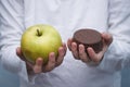 Kid`s hands with chocolate cookie and green apple. Hard choice between healthy and unhealthy food. Royalty Free Stock Photo