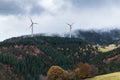 Deciduous and coniferous forest on the hill disappears in the autumn fog, wind mills Royalty Free Stock Photo