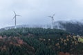 Deciduous and coniferous forest on the hill disappears in the autumn fog, wind mills Royalty Free Stock Photo