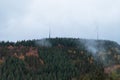 Deciduous and coniferous forest on the hill disappears in the autumn fog, wind mills Royalty Free Stock Photo