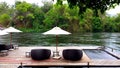 Deck chair or daybeds and umbrellas on waterfront raft in resort near river Kwai Kanchanaburi, Thailand.