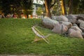 Deck chair standing on green grass at sunset in Garnizon with rocks, trees and blurred people in the background