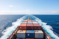 The deck of a massive container ship is shown, with rows of stacked containers towering overhead, as the vessel plows