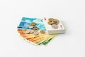 A deck of playing cards with coins lies on a stack of banknotes and coins of new Israeli shekels - NIS - on a white background