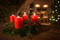 Decorated Advent wreath from fir branches with red burning candles on a dark wooden table, living room with Christmas tree blurred Royalty Free Stock Photo