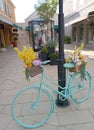 Decorated bicycle with colourful flowers placed next to a pole on the city street