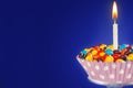 Decorated Birthday cupcake with one lit candle and colorful candies on blue background. Copy space Royalty Free Stock Photo