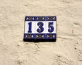 Decorated blue and white house address number 135, hung on a bright, rough wall Royalty Free Stock Photo