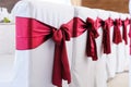 Decorated chairs made of white fabric and large burgundy satin bows. White fabric chair covers stand in a row