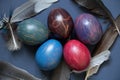 decorated chicken eggs with watercolor multi-colored paints and dove feathers on a blue background, easter prazdnik