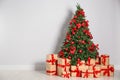 Decorated Christmas tree and gift boxes near light wall Royalty Free Stock Photo