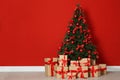 Decorated Christmas tree and gift boxes near red wall Royalty Free Stock Photo