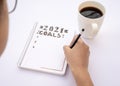 Decorated notebook for writing New Year's resolutions on a table with a coffee cup on the side and a hand writing Royalty Free Stock Photo