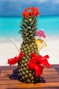 Decorated whole fresh pineapple cocktail with straws, flowers and umbrella on wooden table ocean background at the beach Royalty Free Stock Photo