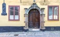 Decorated wooden door framed by stone frame, mediating wooden wrought iron windows in yellow wall and cobblestone floor Royalty Free Stock Photo