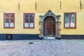 Decorated wooden door framed by stone frame, mediating wooden wrought iron windows in yellow wall and cobblestone floor Royalty Free Stock Photo