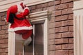 decoration of the facade of Santa Claus on a rope. Santa climbs to the chimney against the background of the window and the brick