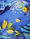 Decorative autumn composition of yellow flowers, leaves, asparagus beans, fruits, colored paper on tinted blue paper