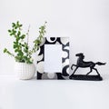 Decorative black and silver picture frame mock up template with spring flowers in white vase and black horse statuette. White