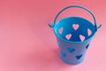 Decorative blue bucket with heart shaped holes on pink background. Festive concept