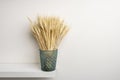 A decorative blue glass container containing a bunch of ears of dried wheat on a white shelf and white wall Royalty Free Stock Photo