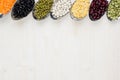 Decorative border of assortment different beans in spoons with copy space on white wood background. Royalty Free Stock Photo