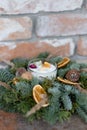 Decorative candle decorated with Christmas tree branches, dried oranges, nuts and cones on a brick wall background Royalty Free Stock Photo