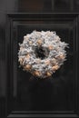 Decorative Christmas wreath covered in artificial snow with illuminated gold colored baubles attached to a green door of a house Royalty Free Stock Photo