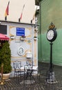 Decorative clock on the leg and table with chairs at the entrance to the cafe on the Cetatii street in a rainy day. Sibiu city in