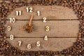Decorative clock with wooden numerals and arrows made of cinnamon sticks, showing 9 o`clock, on a wooden background and a frame of