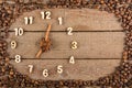 Decorative clock with wooden numerals and arrows made of cinnamon sticks, showing 7 o`clock, on a wooden background and a frame of