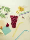 Decorative composition - a glass of fresh raspberries, cocktail tubules, fresh flowers, petals and berries on a light background