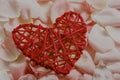 Decorative coral wooden heart made of rattan on pink rose petals background. Selective focus Royalty Free Stock Photo